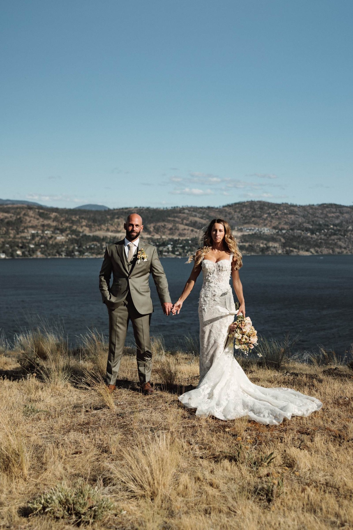 Bride and groom standing together on the hillside above the lake