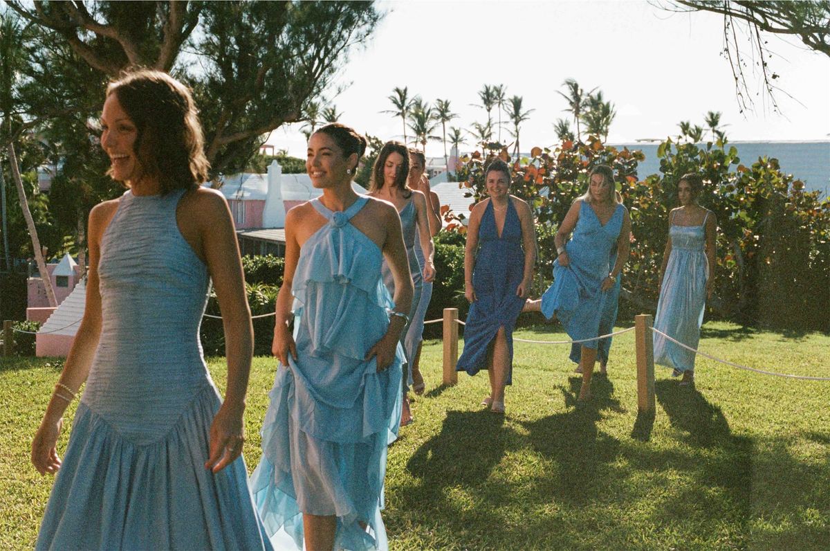 Bridesmaids in blue dresses walking across the sunlit lawn together