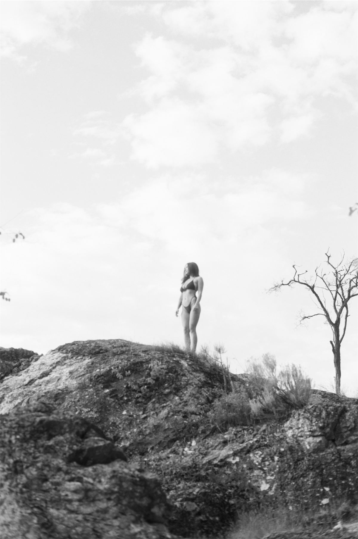 Black and white frame of a lone figure standing on a rocky outcrop under open sky