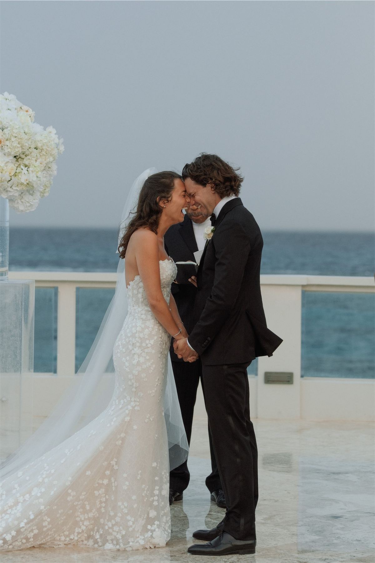 Foreheads together on an oceanfront deck beside towering white hydrangeas
