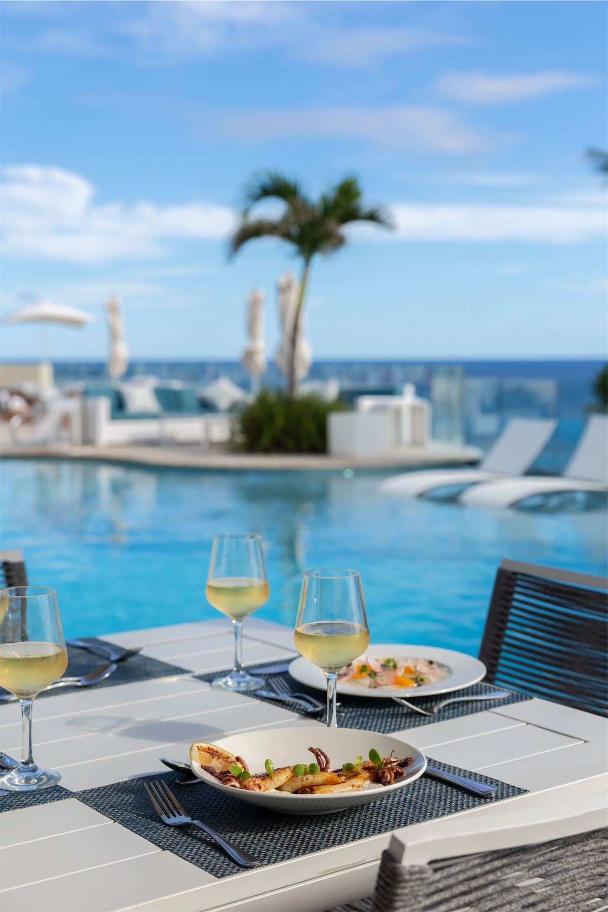 Poolside table set with wine and lunch beside an infinity pool and palm trees