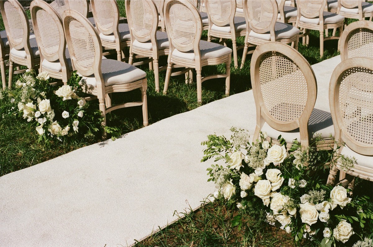 Empty cane ceremony chairs lining an aisle edged with white and green florals