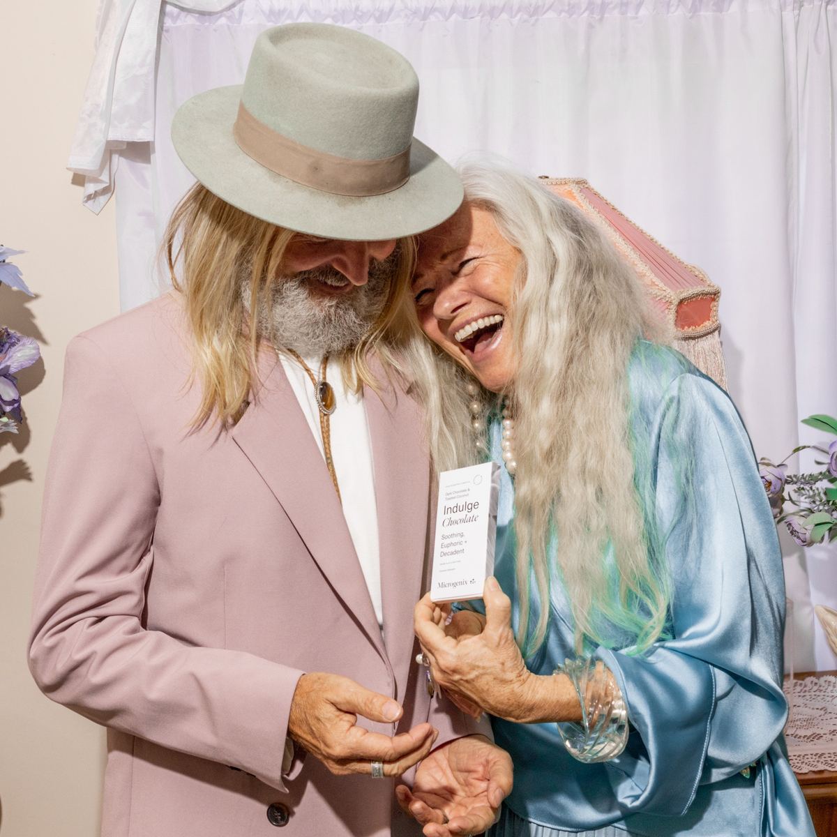 Older couple in pastel tailoring laughing together with a chocolate bar in hand