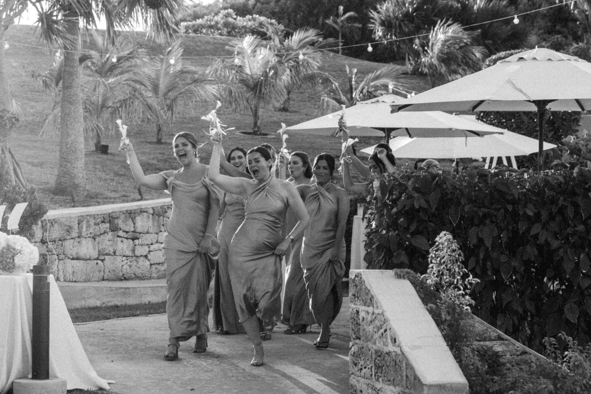 Bridesmaids dance into the reception under the umbrellas on Hawkins Island, Bermuda, black and white