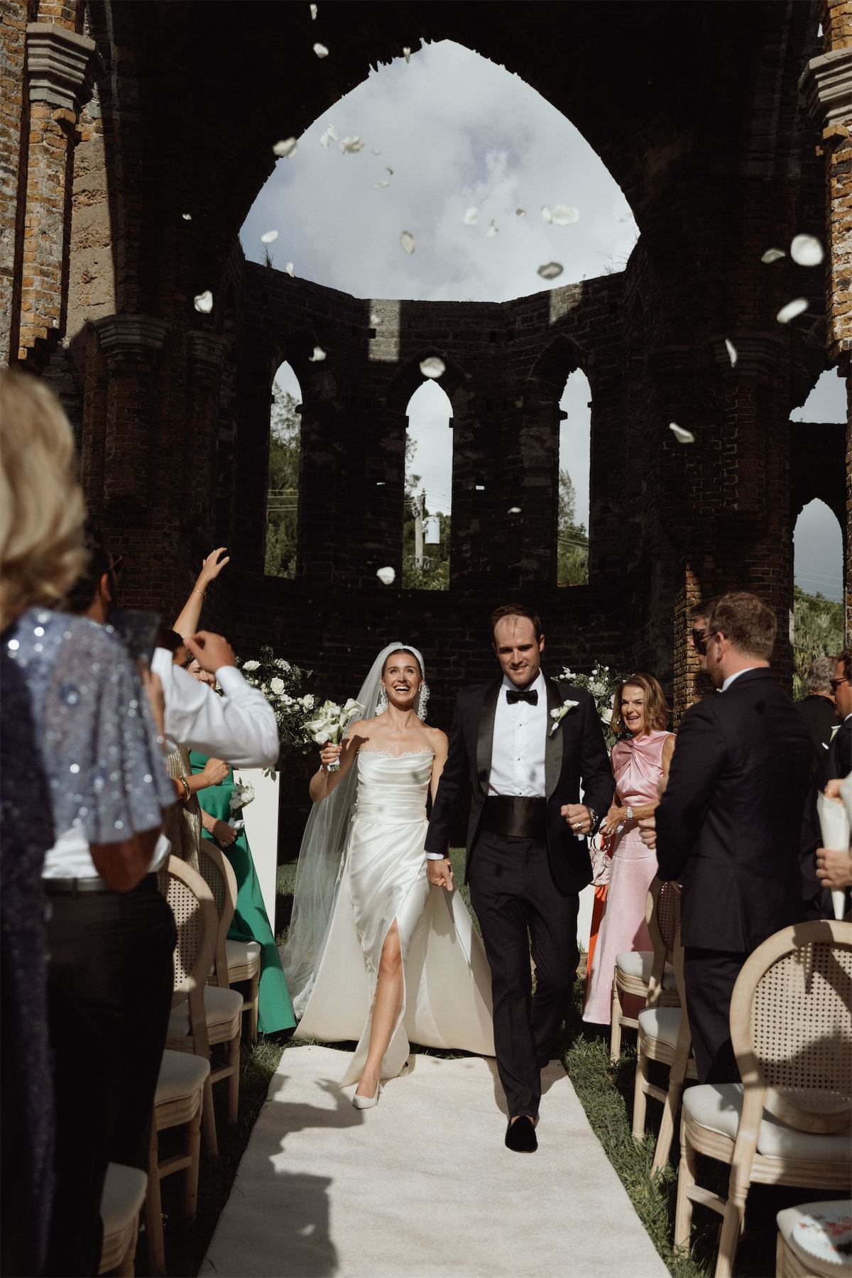 Bride walking the aisle on her father's arm inside roofless stone church ruins