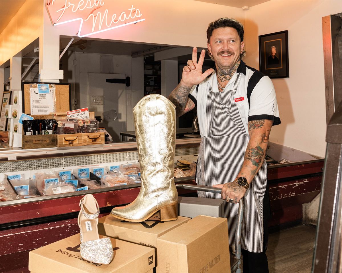 Butcher throwing a peace sign behind the counter beside gold cowboy boots on boxes