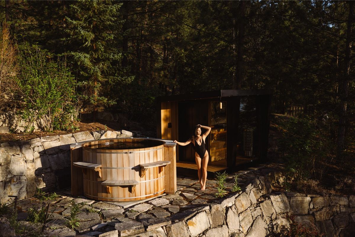 Cedar hot tub and sauna on a stone terrace with a woman in the doorway