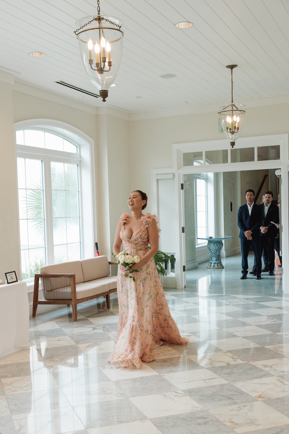 Bridesmaid in a blush gown walking down the checkered marble aisle at Rosewood Bermuda