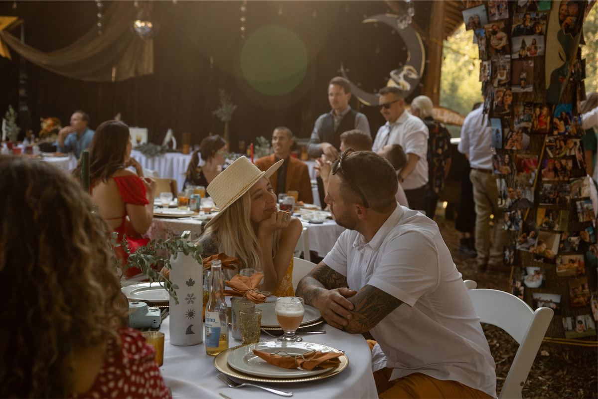 Guests eating and talking at long reception tables under a rustic pavilion