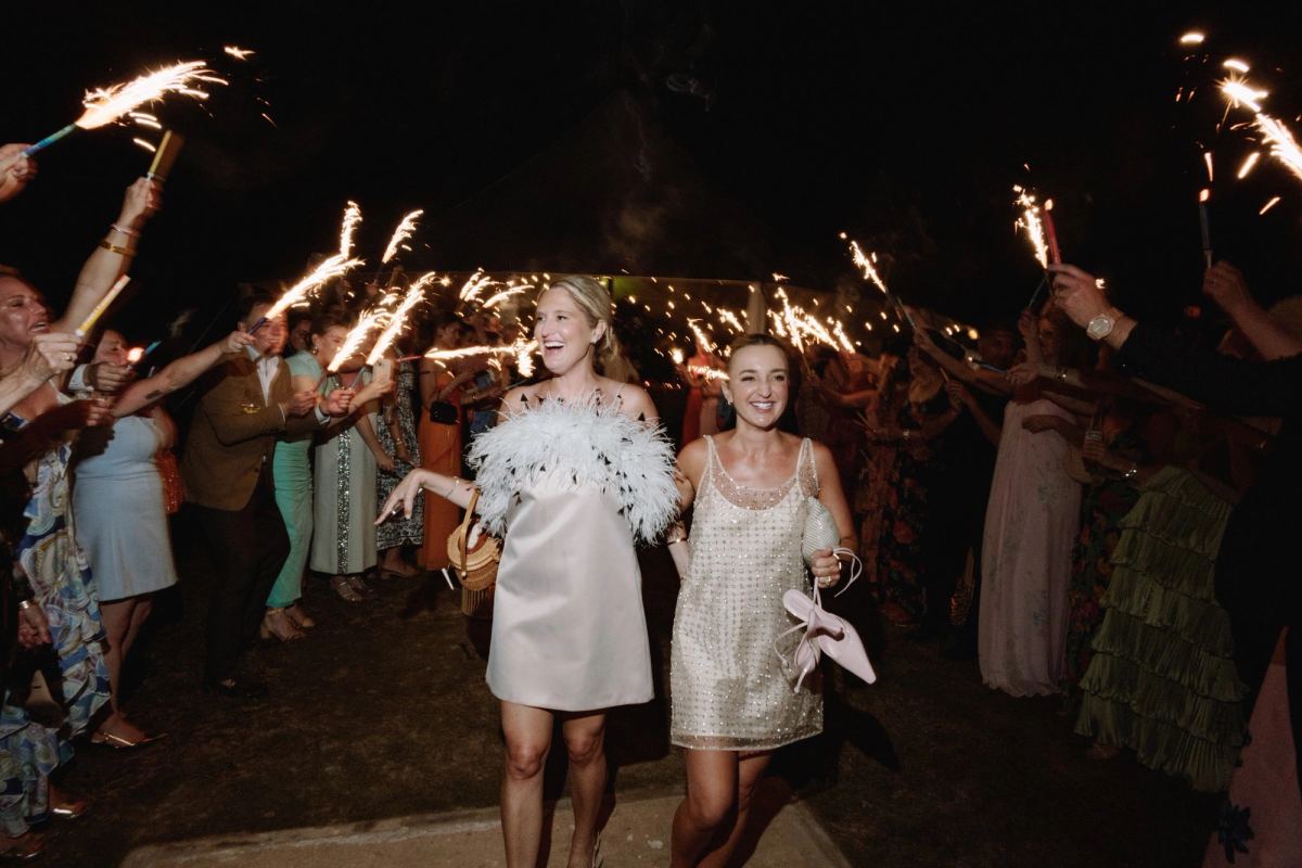 Two brides laughing as they run through a sparkler exit at their Bermuda wedding