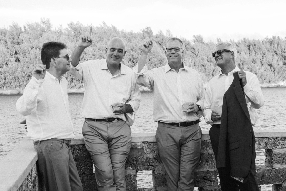 The dads dance by the sea wall with jackets in hand on Hawkins Island, Bermuda, black and white