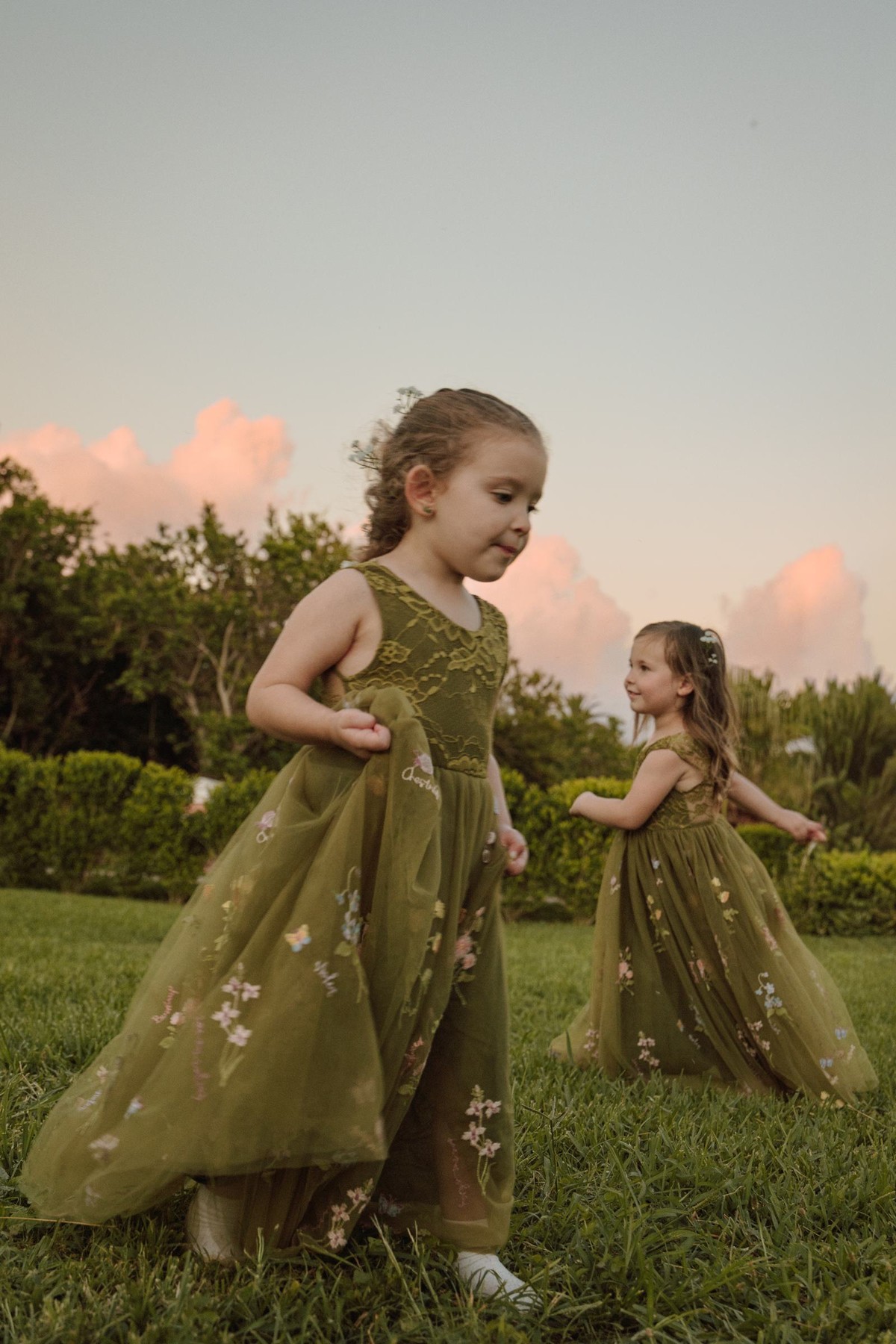 Flower girls in green twirling on the lawn at sunset