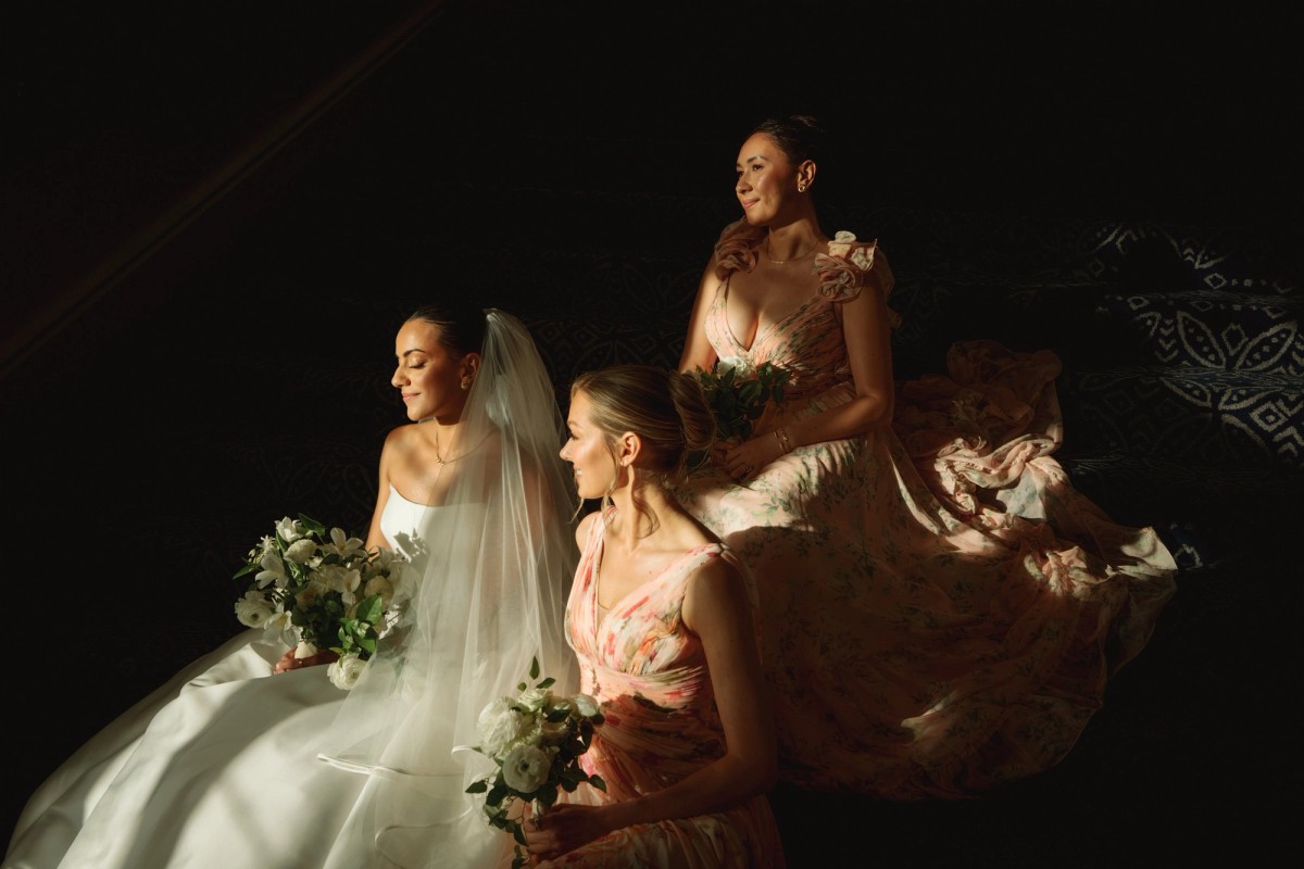 Bride and bridesmaids lit by a single shaft of light on the staircase at Rosewood Bermuda