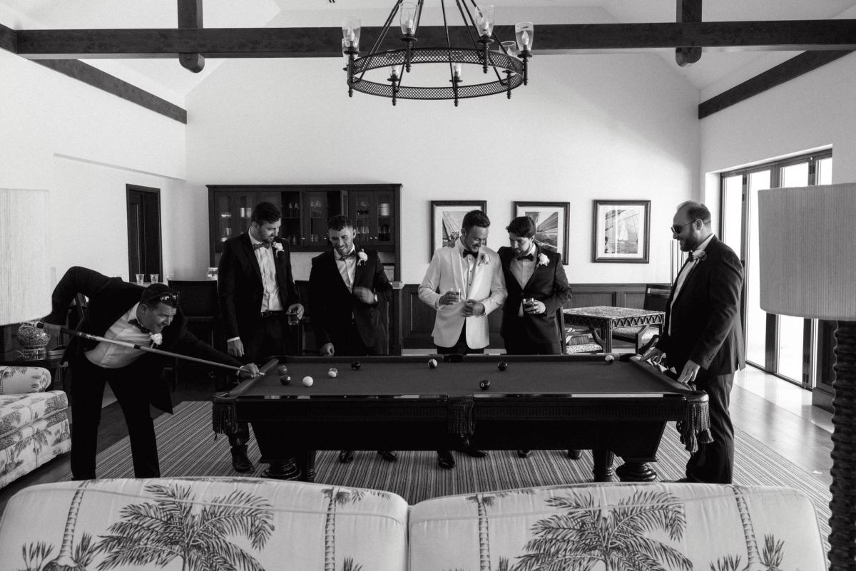 Groom and groomsmen relaxing around pool table during wedding day prep