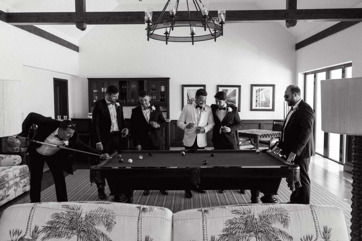Groom and groomsmen relaxing around pool table during wedding day prep