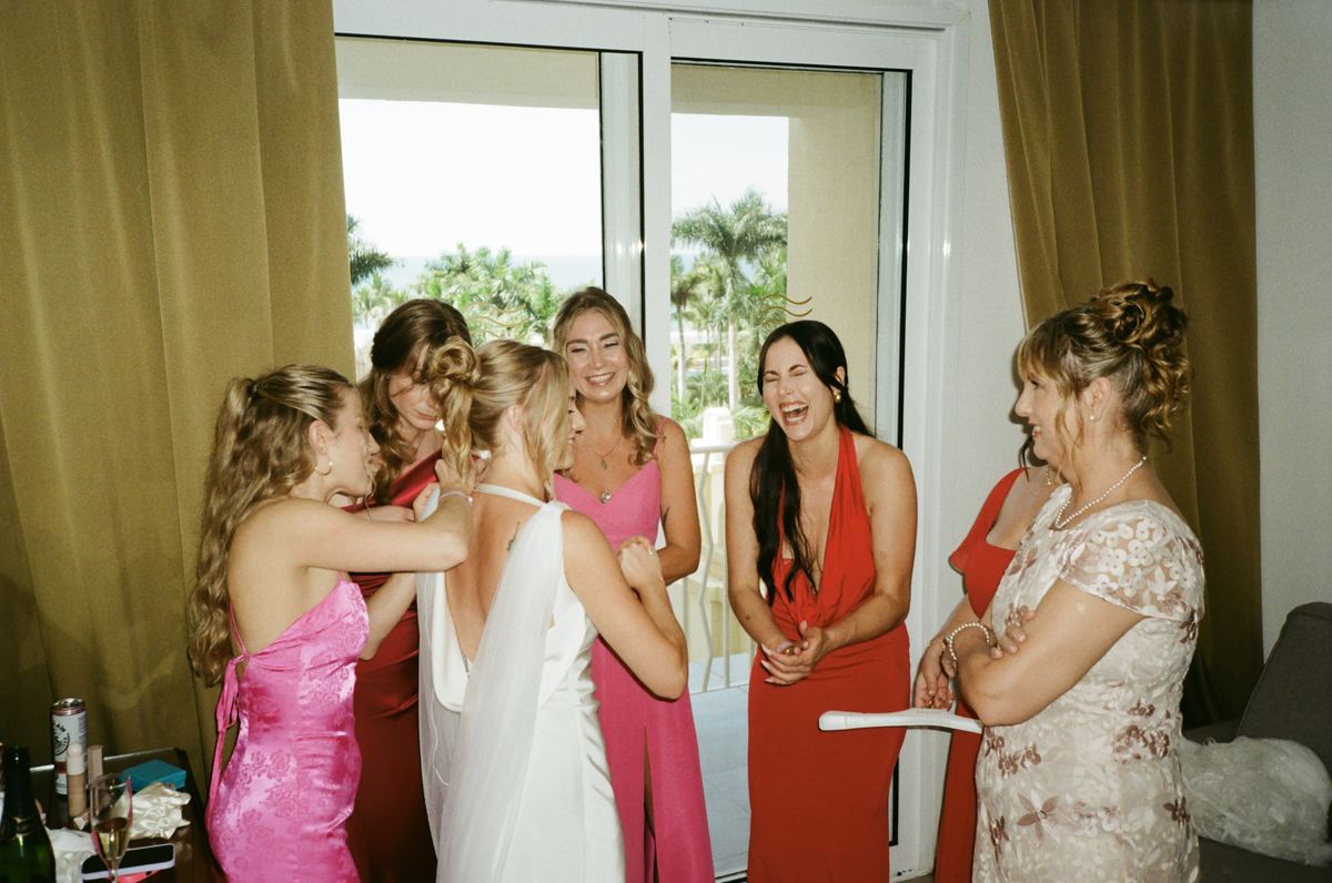 Bridesmaids laughing with bride in getting ready room with palm trees through window