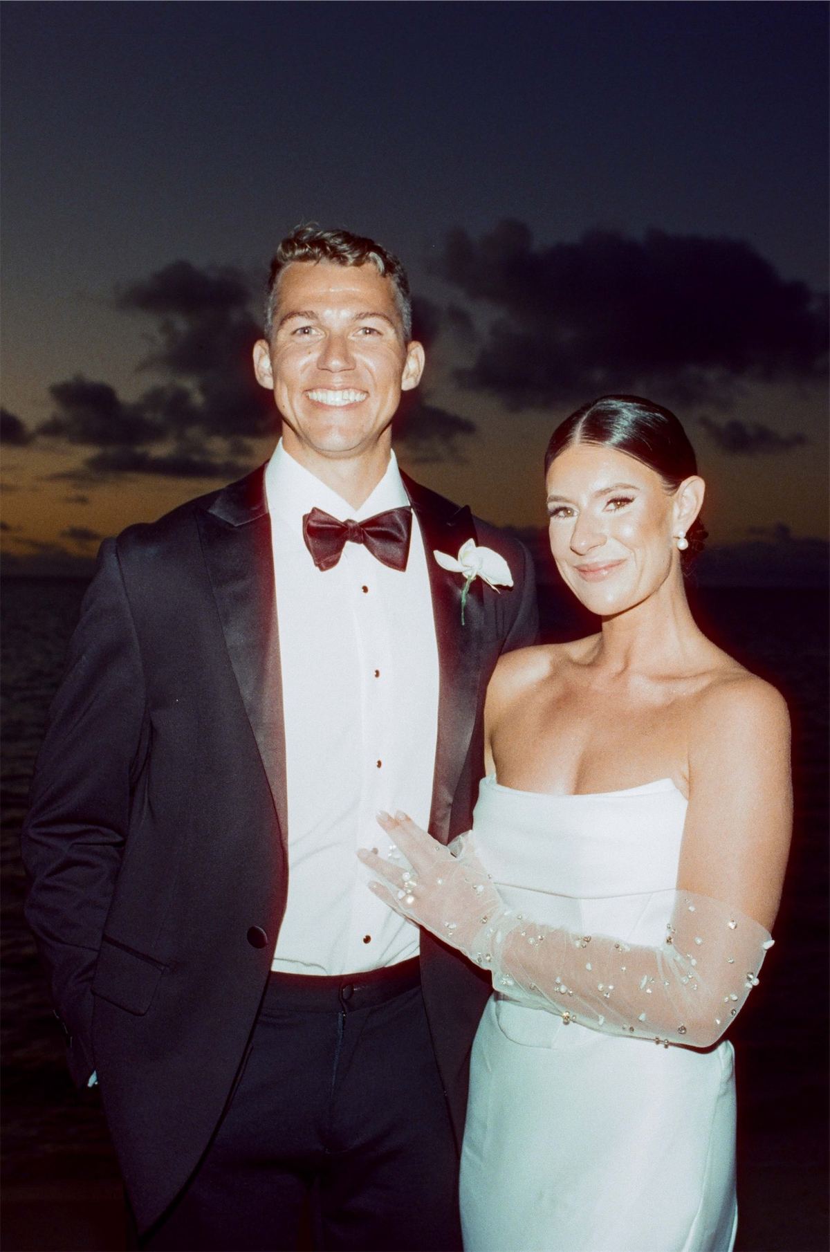 Bride and groom posing together against deep blue twilight over the ocean