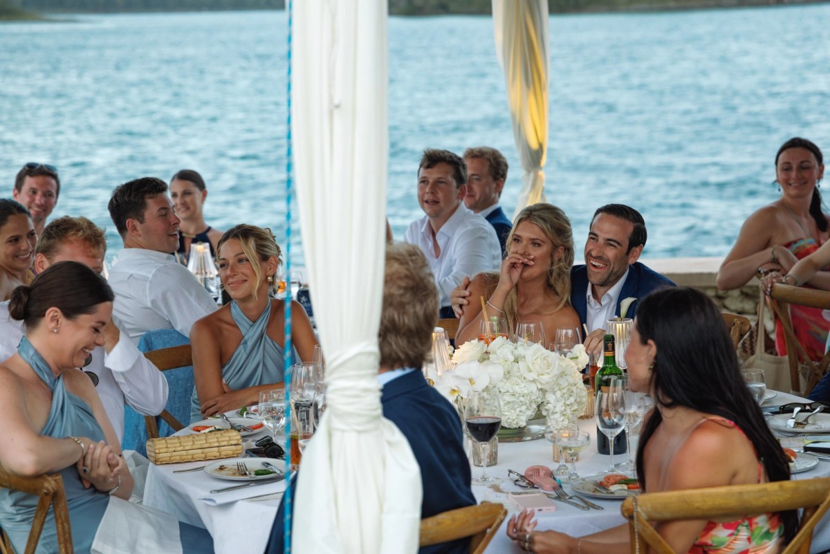 Guests laugh around the dinner table by the water on Hawkins Island, Bermuda