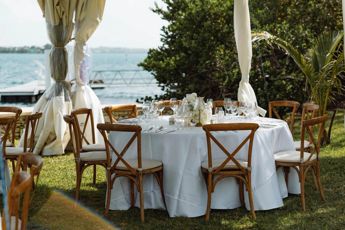 Reception tables set beside the water under draped tent poles on Hawkins Island, Bermuda