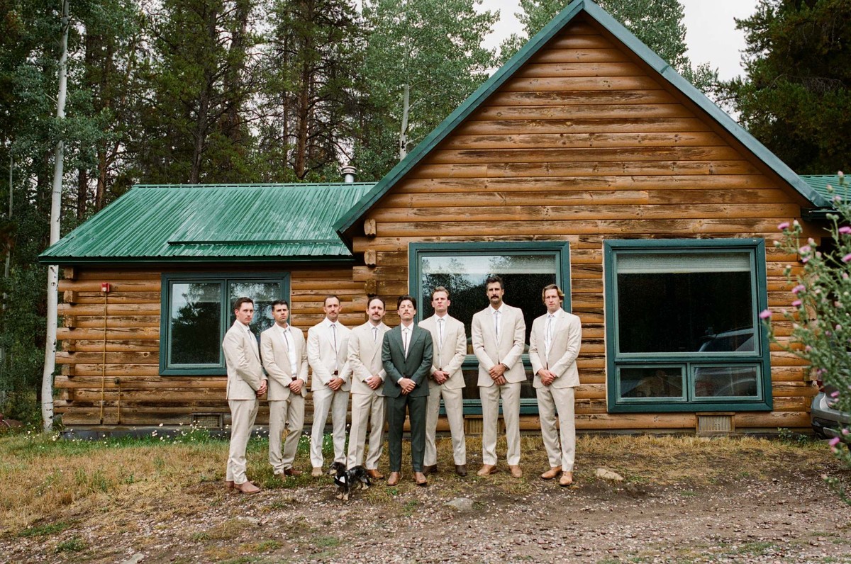 Owen and his groomsmen in front of the green roofed log cabin with the dog, shot on film at a mountain ranch among the aspens