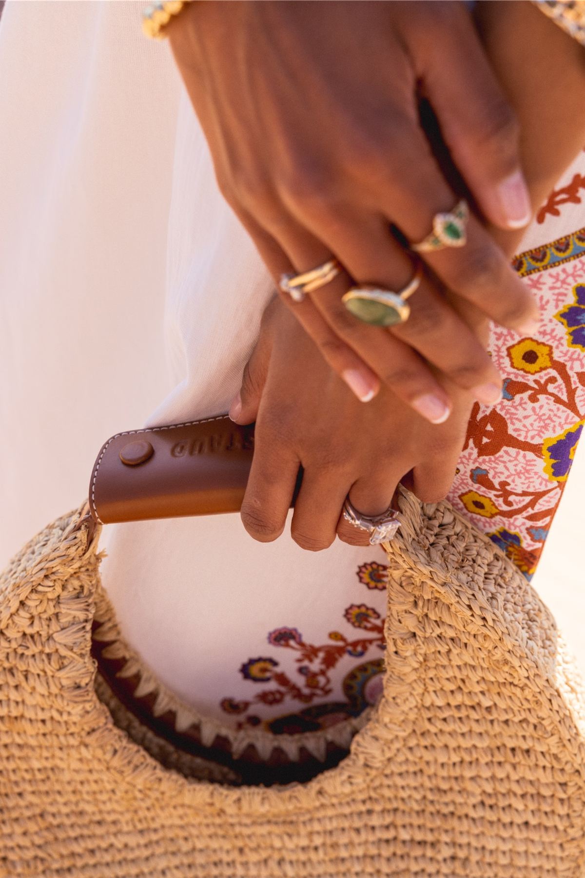 Detail of gold rings on a model's hands resting on a woven straw bag
