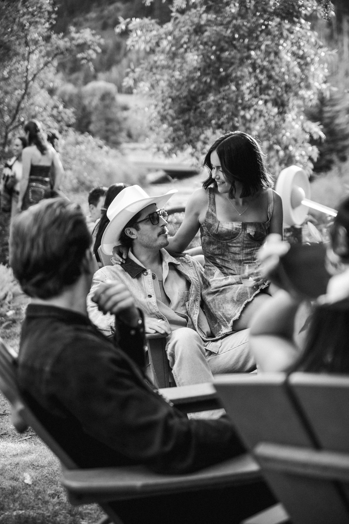 Devin leans in to talk with friends on the garden chairs at a mountain ranch among the aspens, black and white