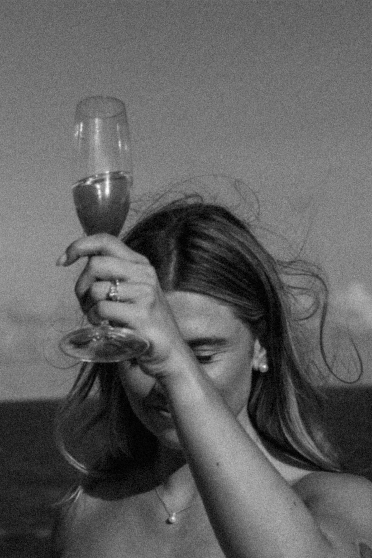 Black and white shot of a guest tipping back a champagne coupe in the beach wind