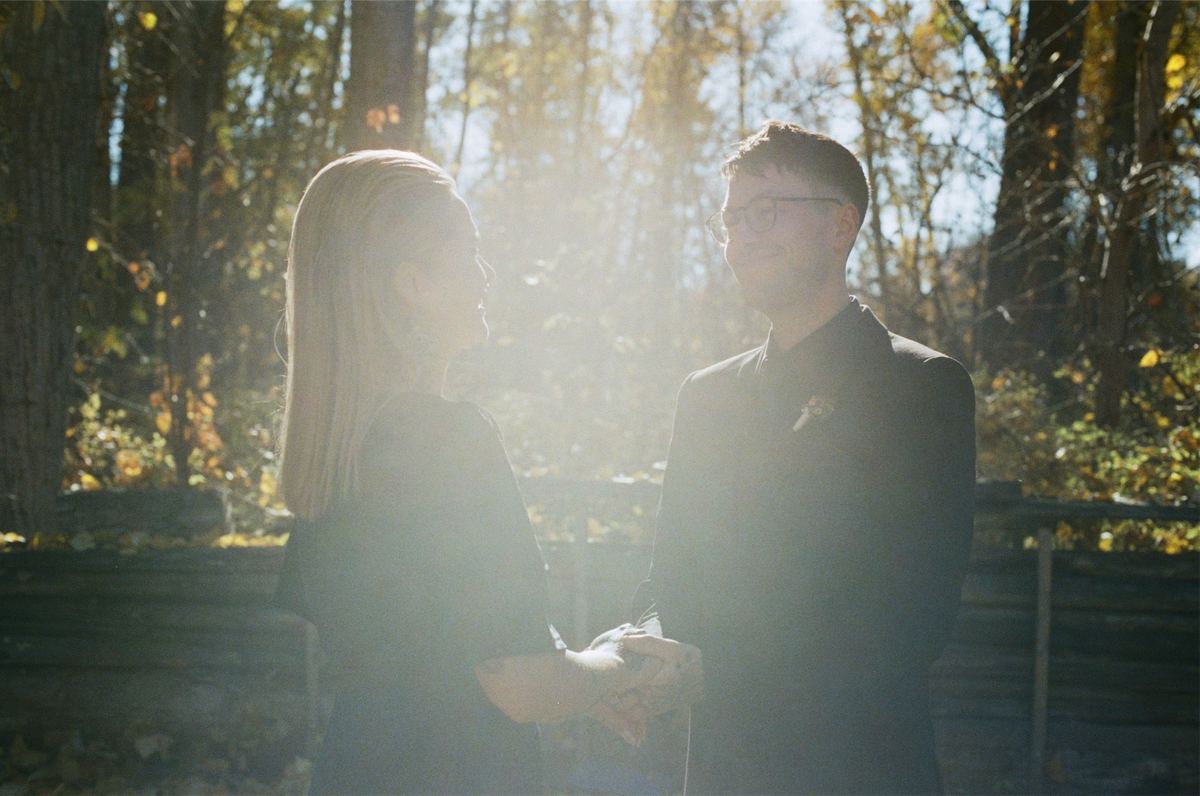 Bride and groom facing each other in backlit late sun among the trees