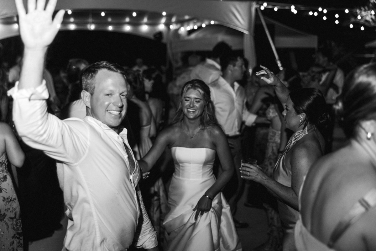 A guest throws his hand up next to Paige on the packed dance floor on Hawkins Island, Bermuda, black and white