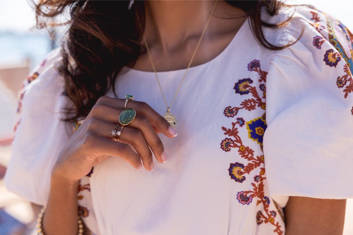 Close crop of an embroidered white blouse layered with gold pendant necklaces and rings