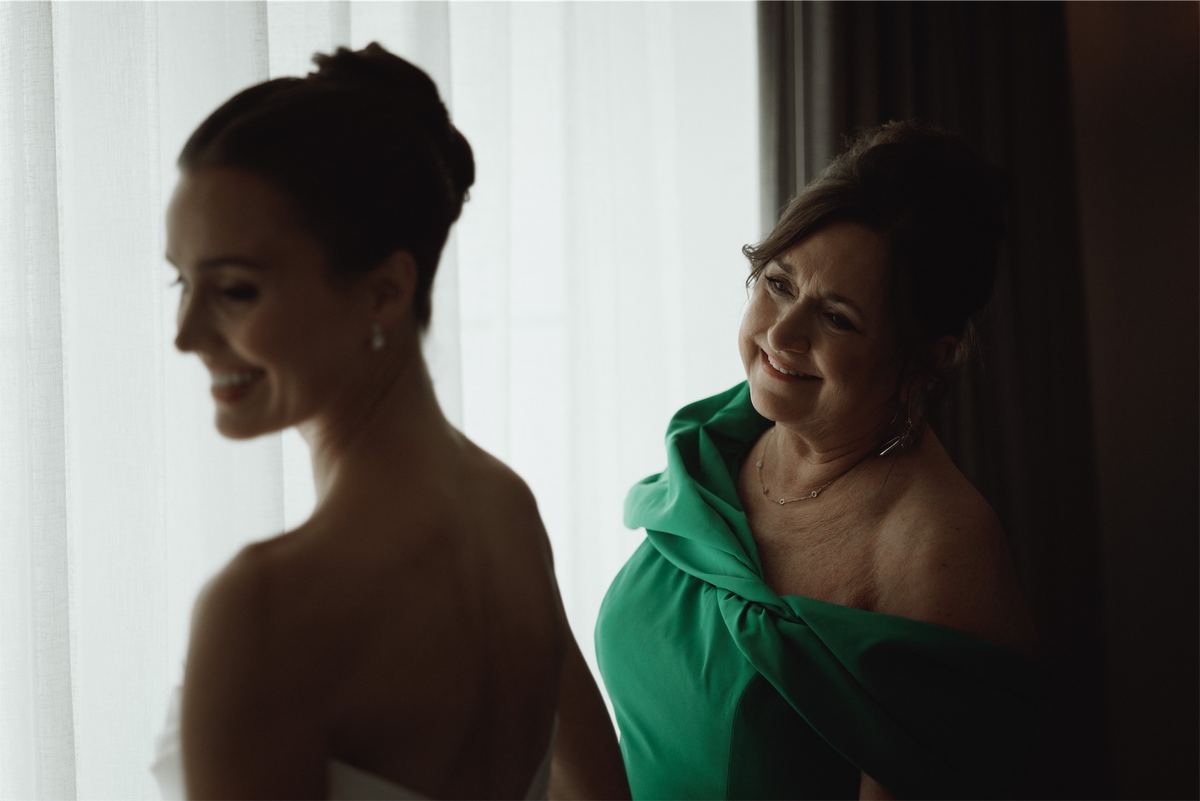 Bride and her mother in green laughing together in the window light