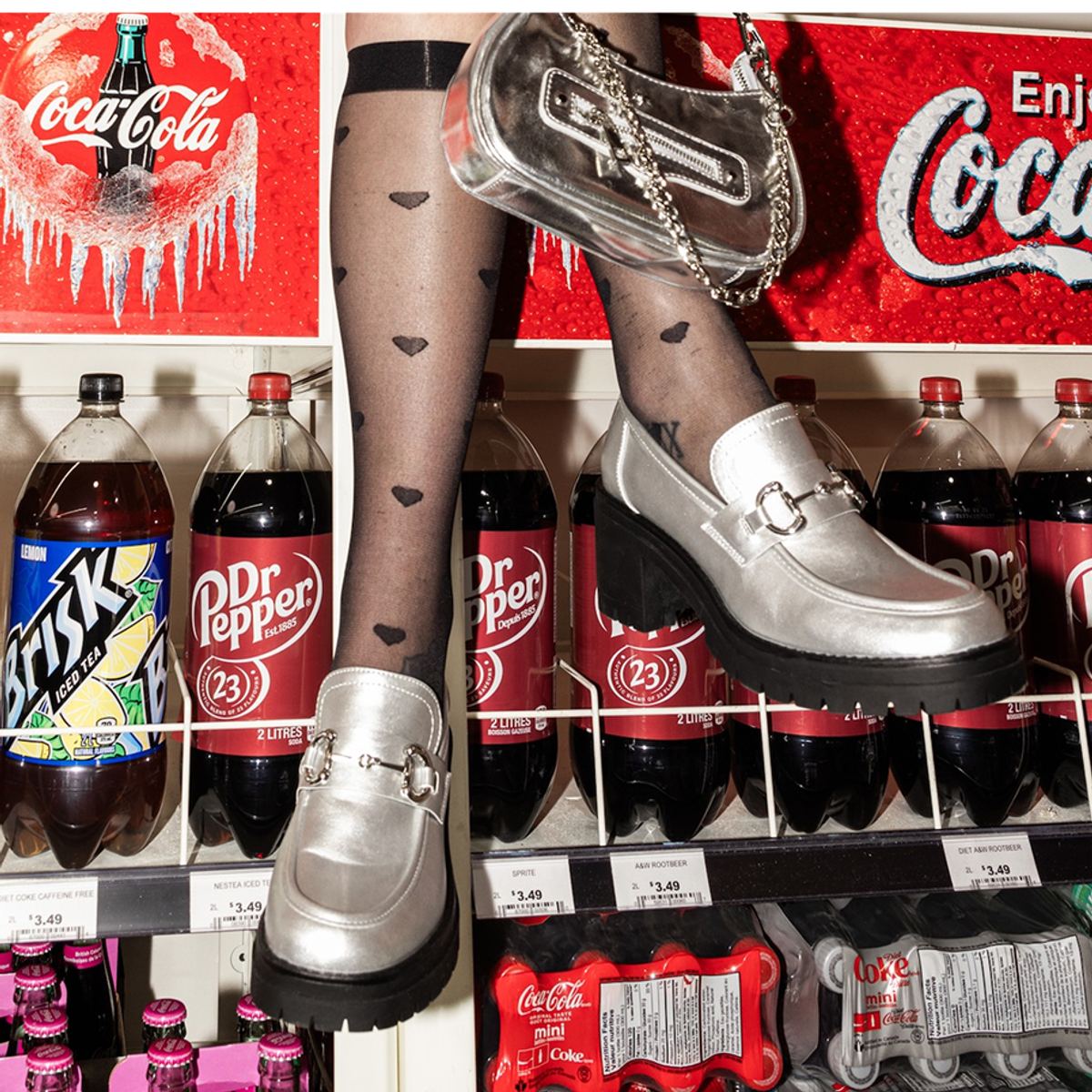 Detail of silver loafers and printed tights in front of a wall of soda bottles