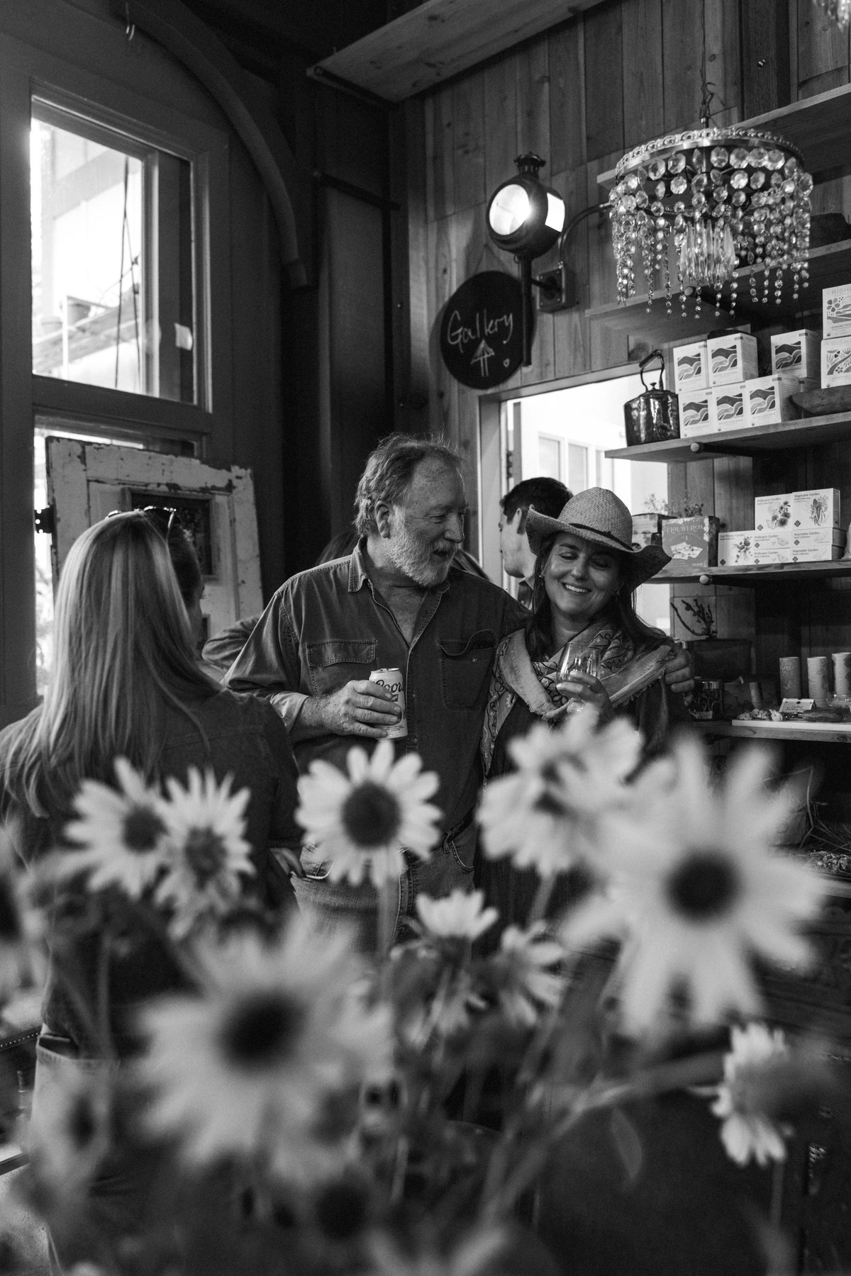 Guests talk by the shop counter behind a vase of sunflowers at a mountain ranch among the aspens, black and white
