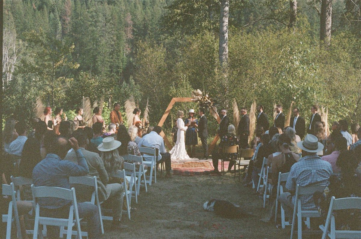 Wide view of the forest ceremony with guests seated on white folding chairs