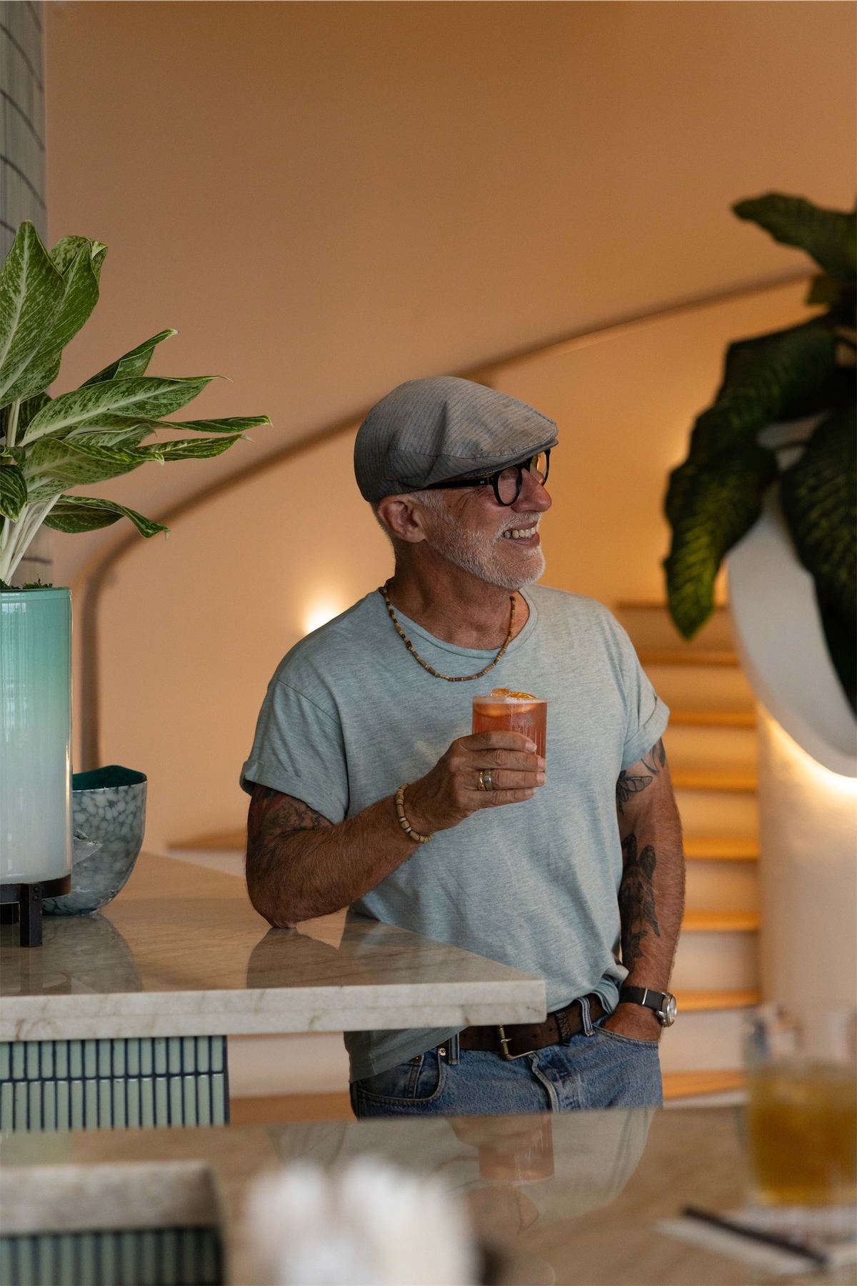 Man in a flat cap laughing over a drink at the indoor bar