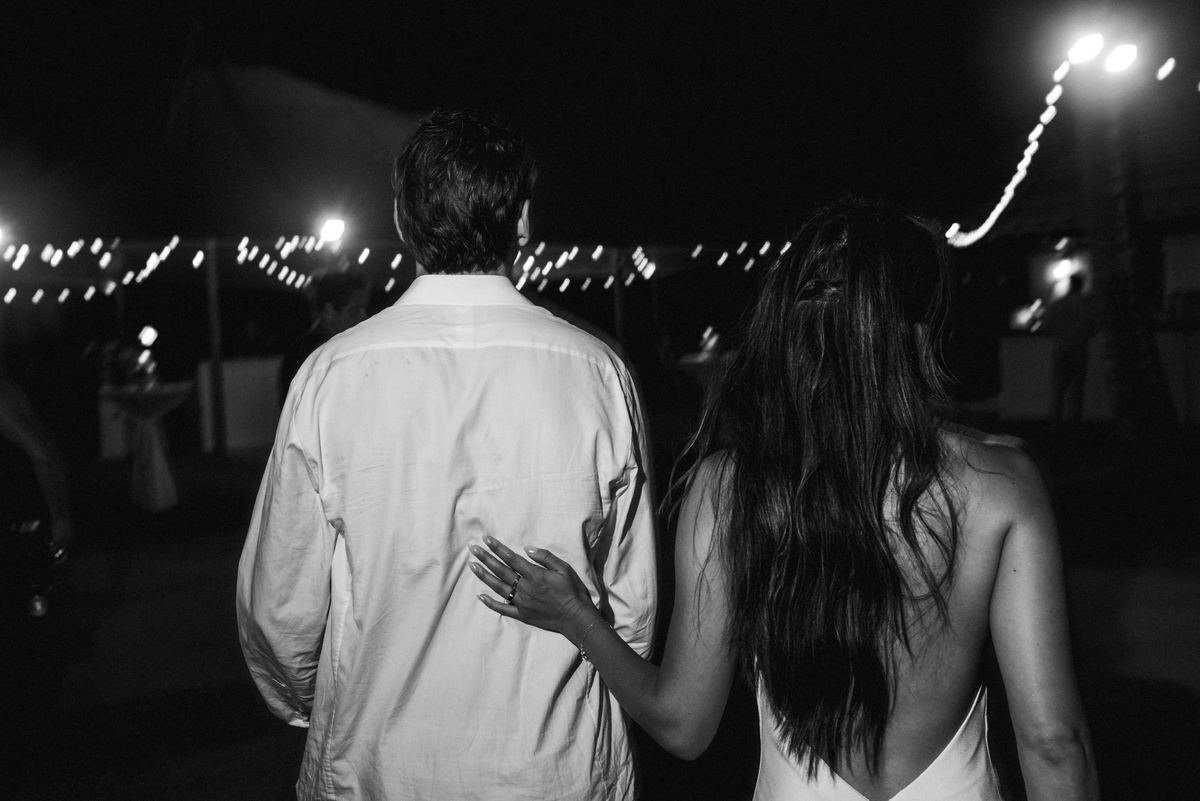 Black and white photograph of the couple walking away together under the string lights