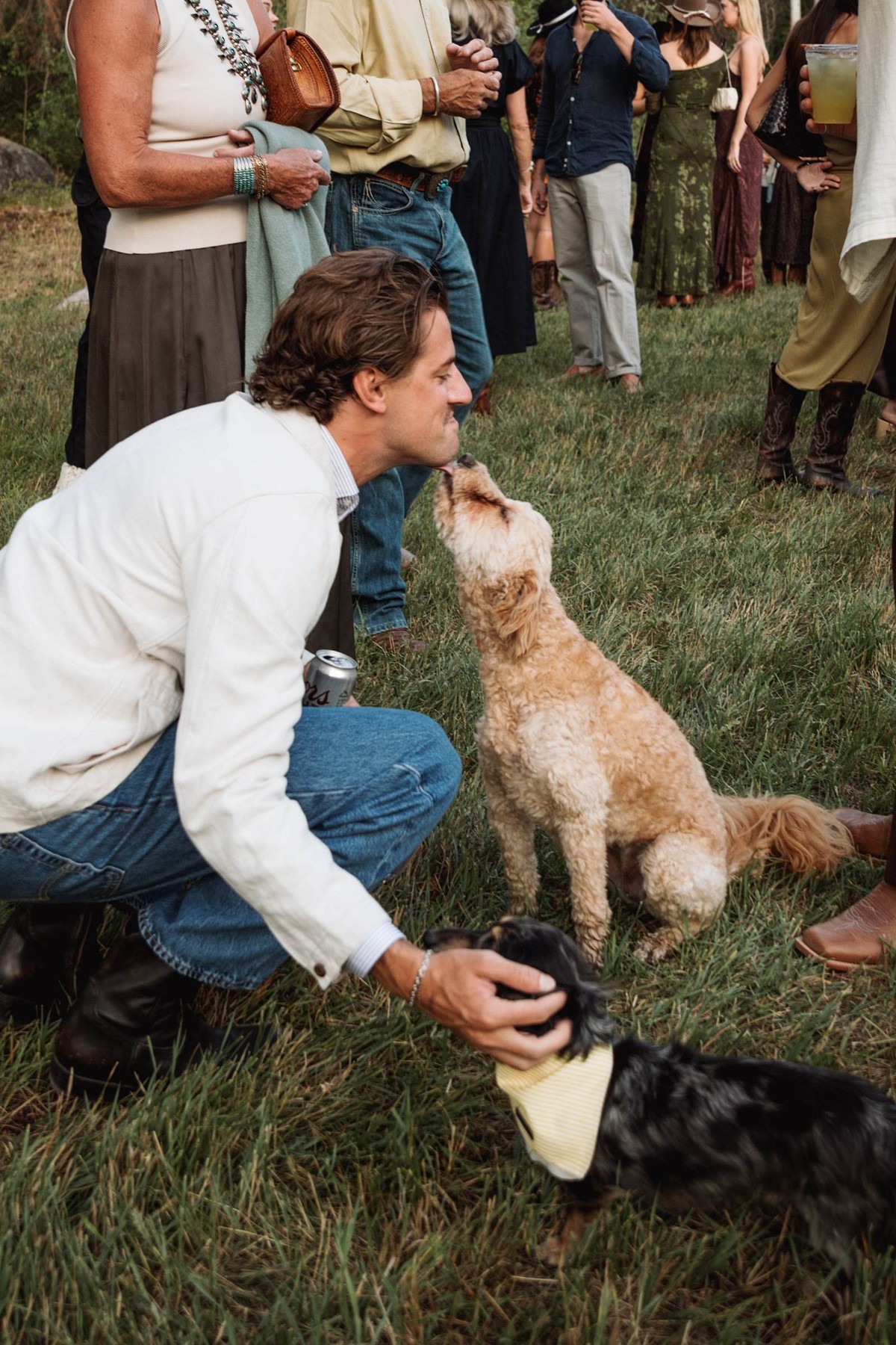 A guest crouches to greet the two dogs at the welcome party at a mountain ranch among the aspens