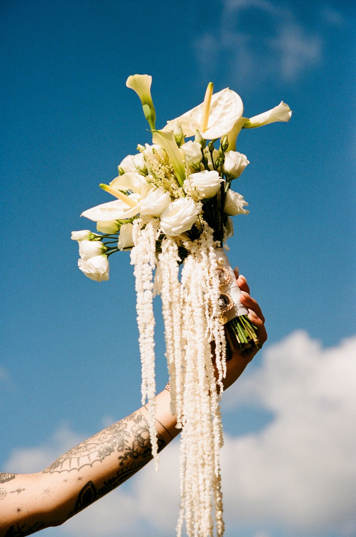 Bride holding her white calla lily bouquet up against a blue Bermuda sky, shot on film