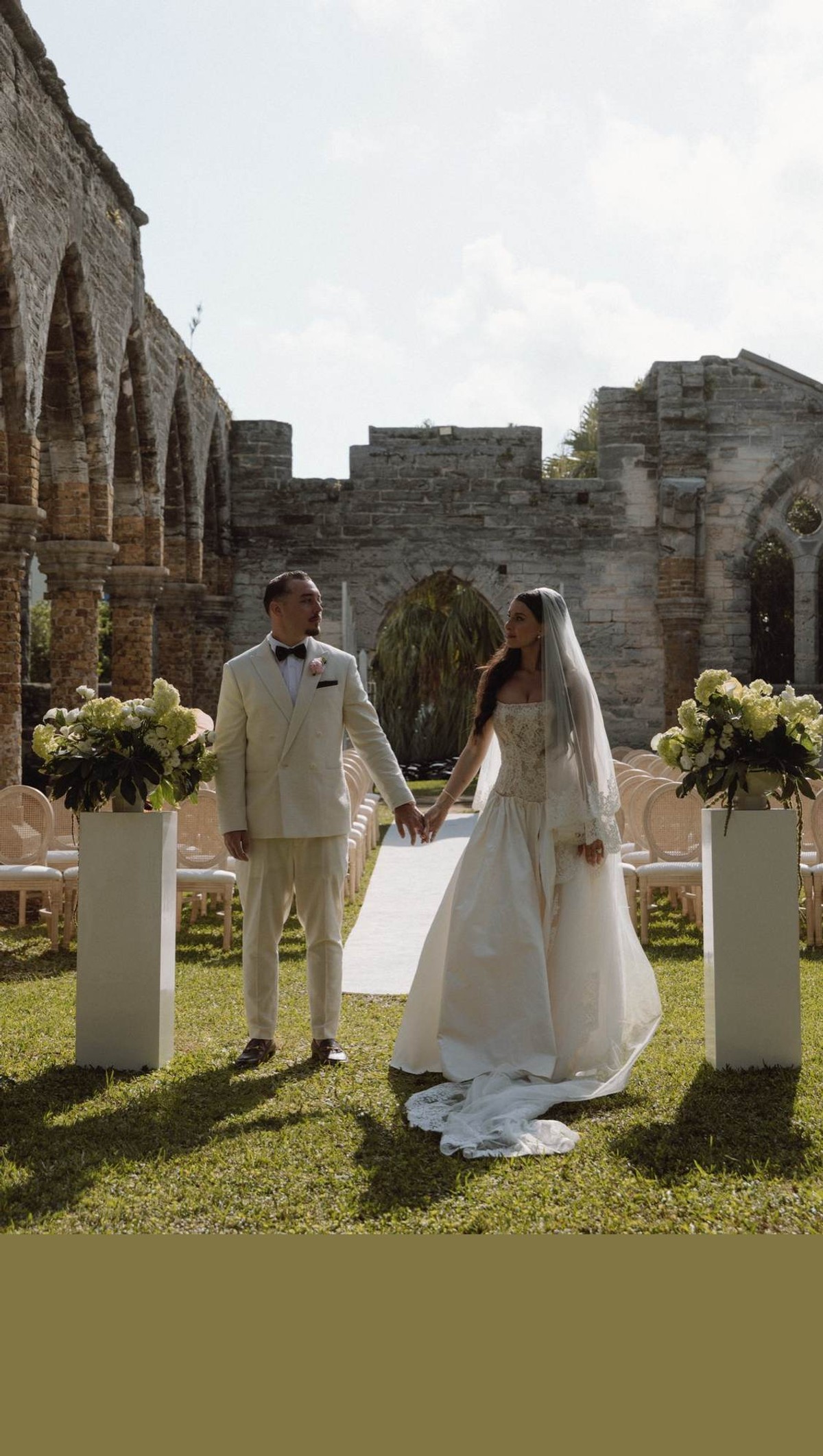Romantic couple holding hands between floral pedestals at Bermuda ceremony