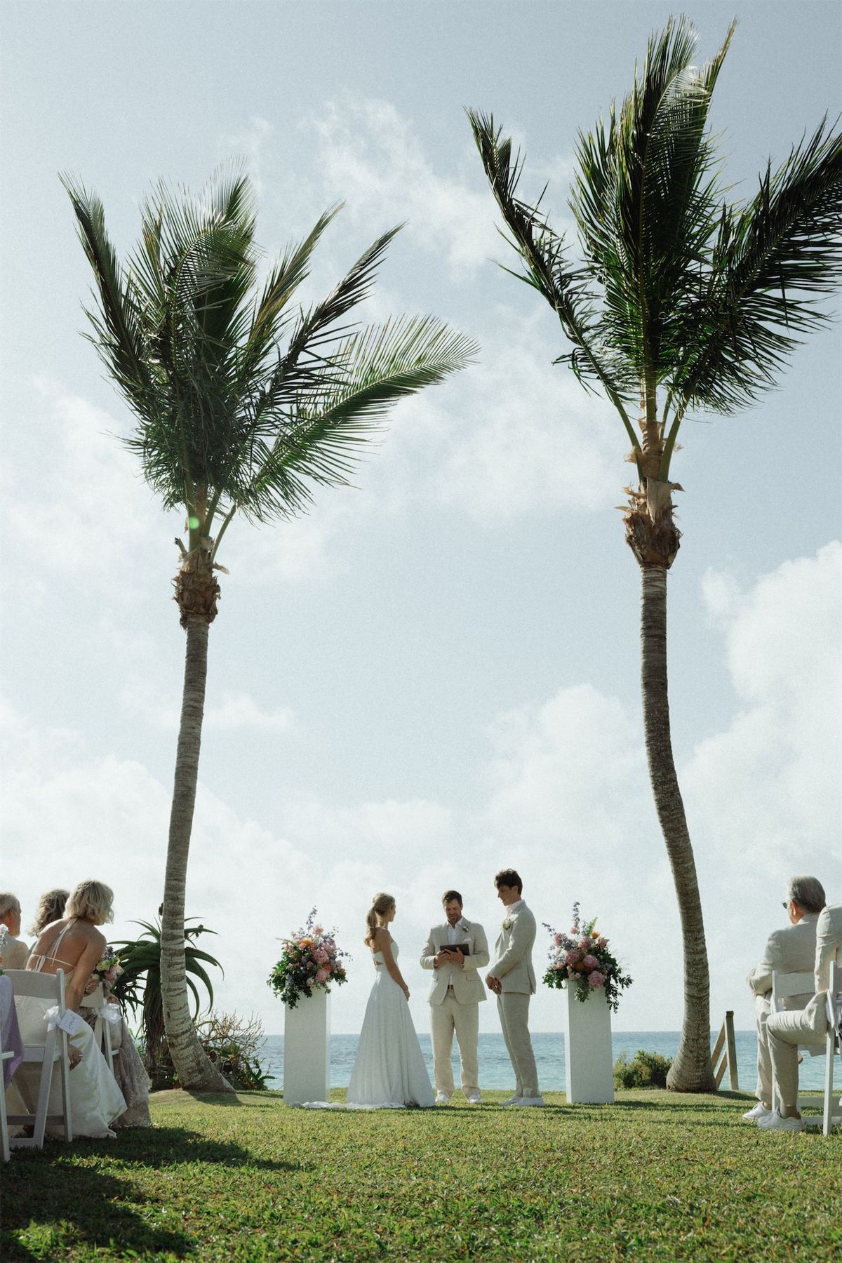 Wide view of the ceremony held beneath two tall palms on an oceanfront lawn