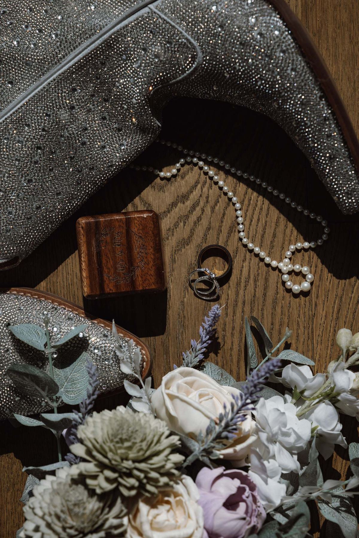 Flat lay of glitter cowboy boots, rings and the bridal bouquet on a wood floor