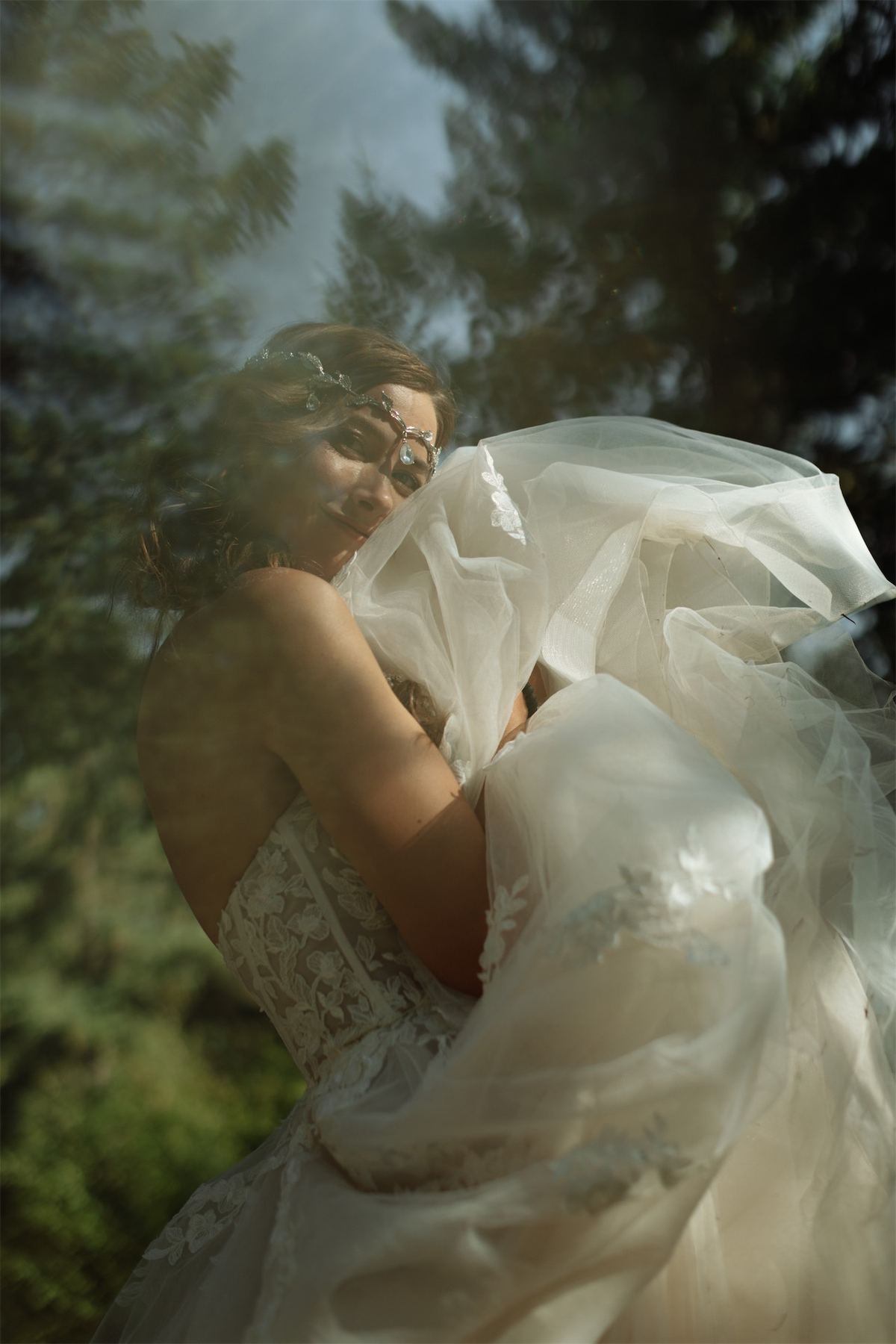 Bride's veil lifting in the breeze as the two stand among the pines