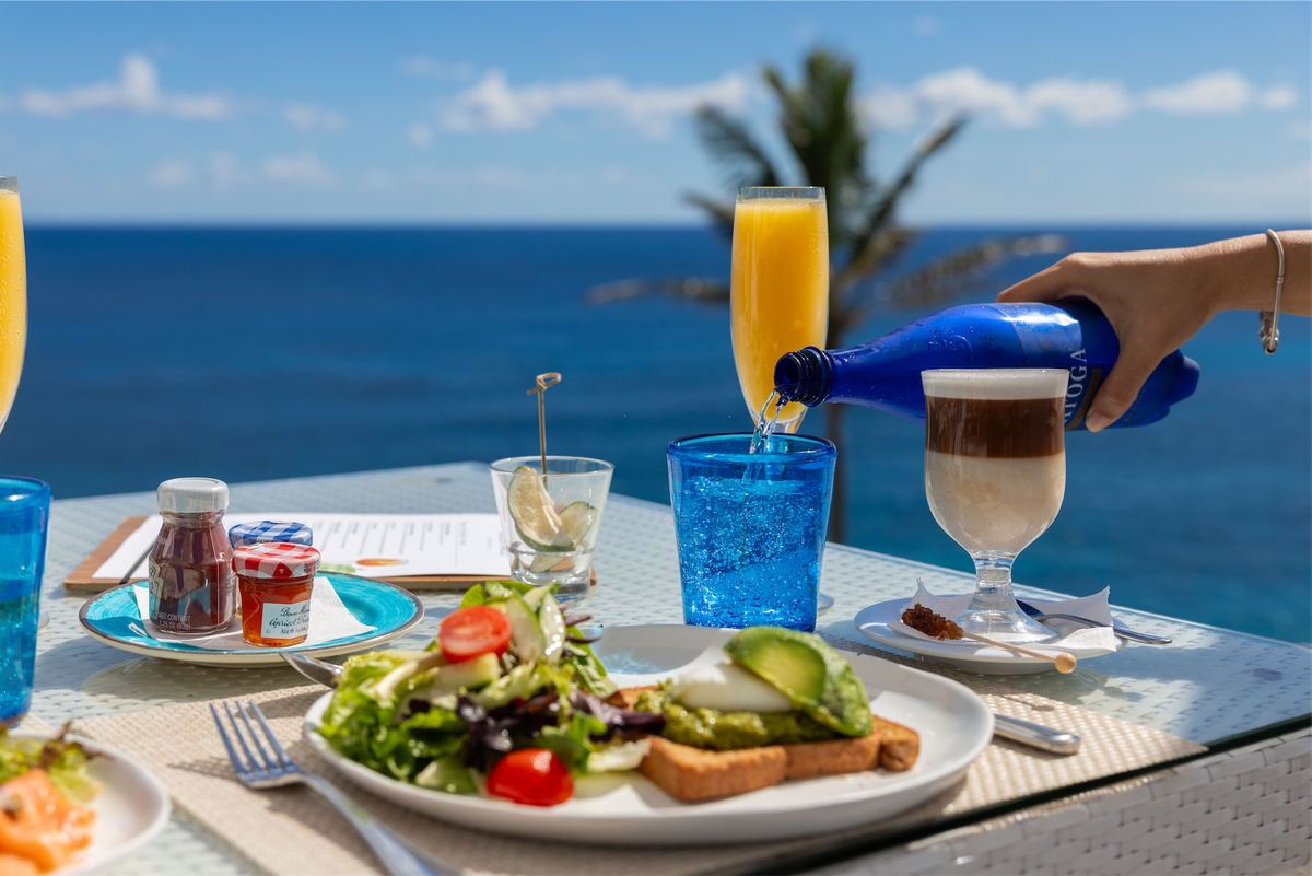 Breakfast of salad, avocado toast and mimosas laid out on an oceanfront table