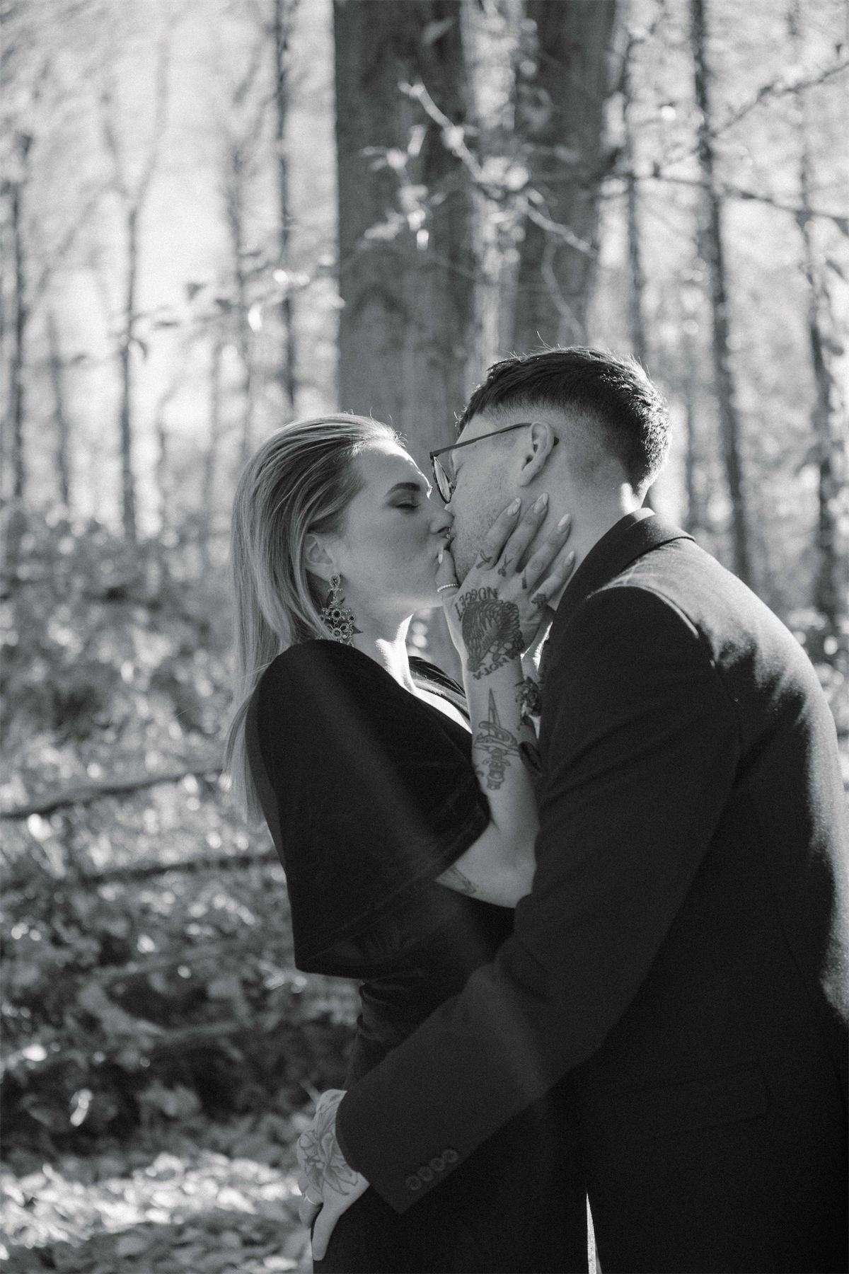 Black and white kiss between the newlyweds in a sunlit birch wood