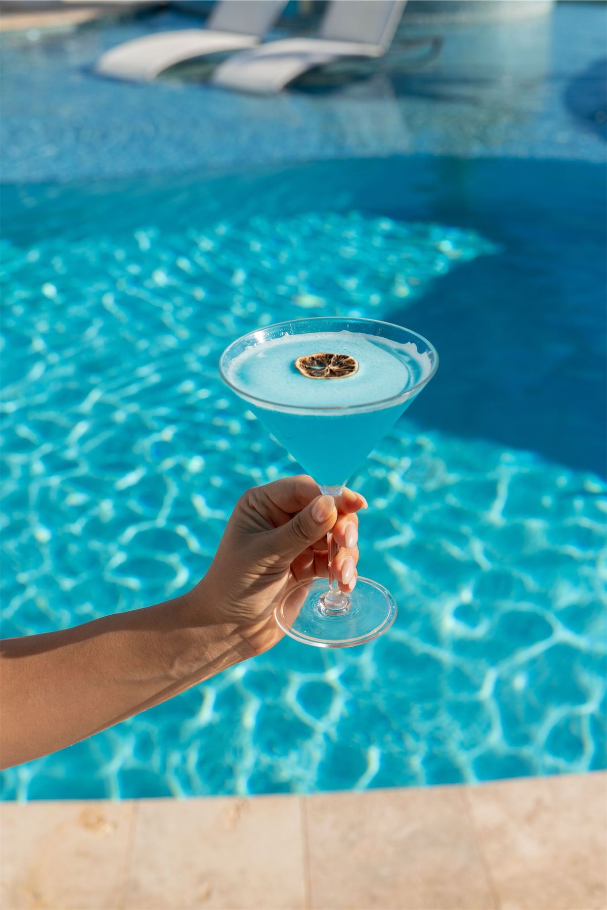 Hand holding a small plate of canapes out over the sunlit pool water