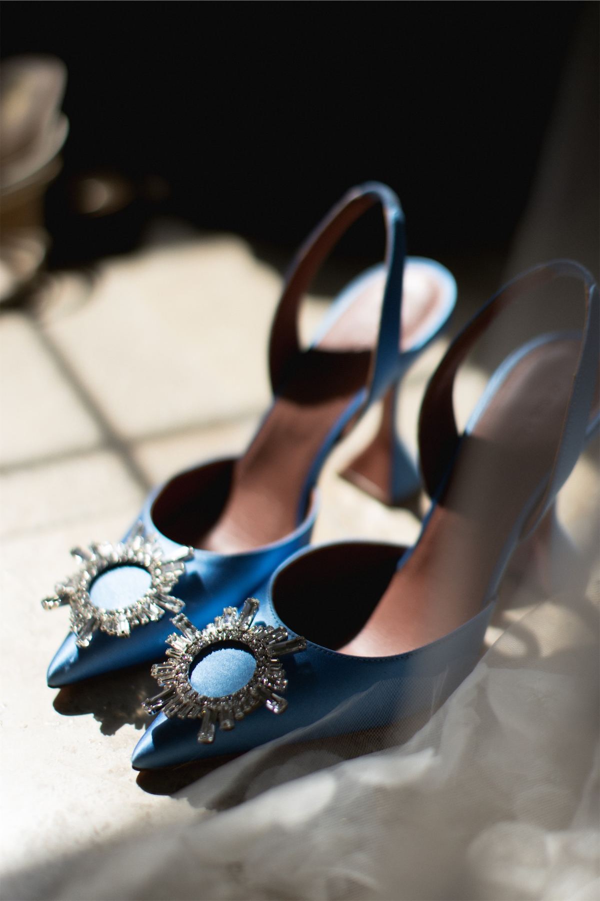 Blue satin heels with jewelled buckles resting on the bride's dress