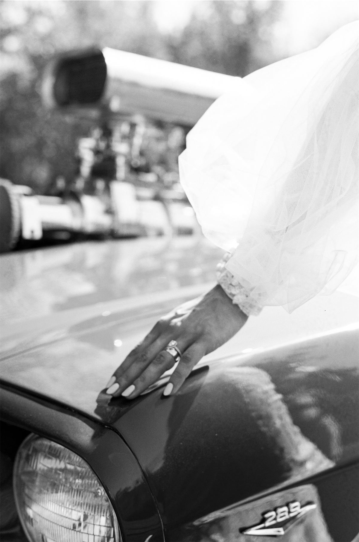 Black and white detail of the bride's ringed hand resting on a classic car