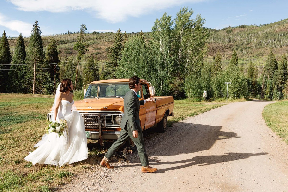 Devin and Owen walk around the orange vintage pickup on the dirt road at a mountain ranch among the aspens