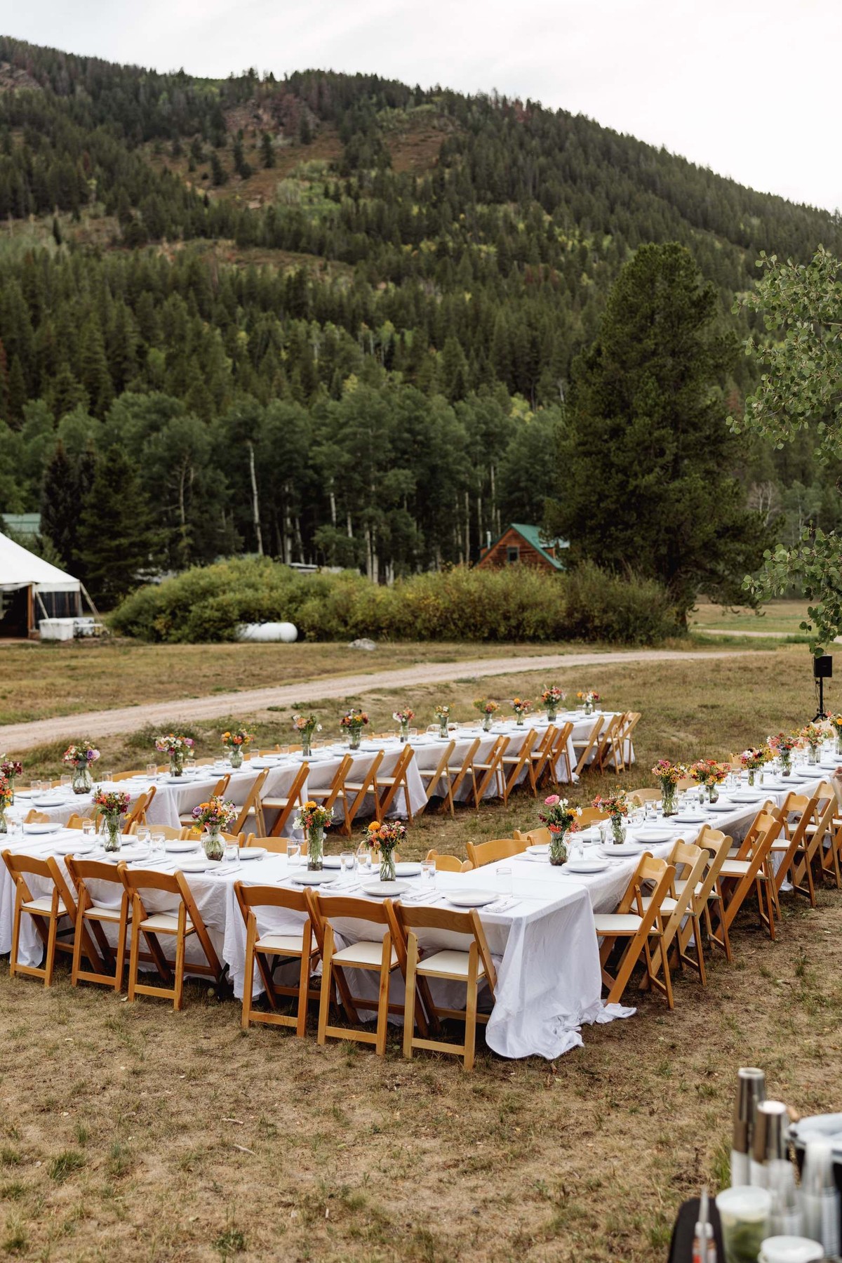 Long welcome party tables set in a field below the mountain at a mountain ranch among the aspens
