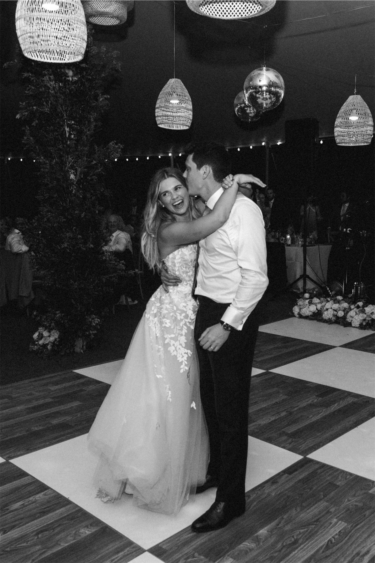 Black and white of the newlyweds dancing on a checkerboard floor beneath disco balls